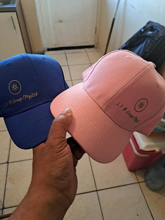 A navy cap and a pink cap printed with the L and M Group company logo