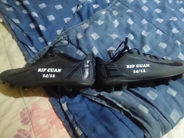 Black football boots printed in memory of a young player, each boot carrying his name and a date
