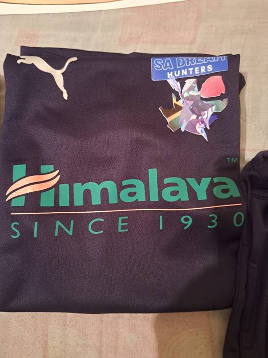Navy team shirt printed with a sponsor logo and an SA Dream Hunters badge over the South African flag