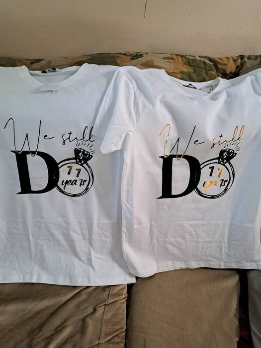 Two white anniversary t-shirts printed We Still Do around a ring marked eleven years, one in black and one in gold foil